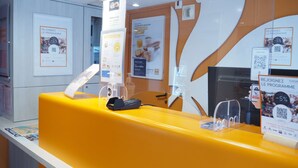 A reception desk with a yellow counter, a payment terminal, and informational posters on the wall. - Premiere Classe Saumur (Saumur)