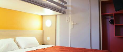 A hotel room with a bed, a wardrobe, and a red wall.