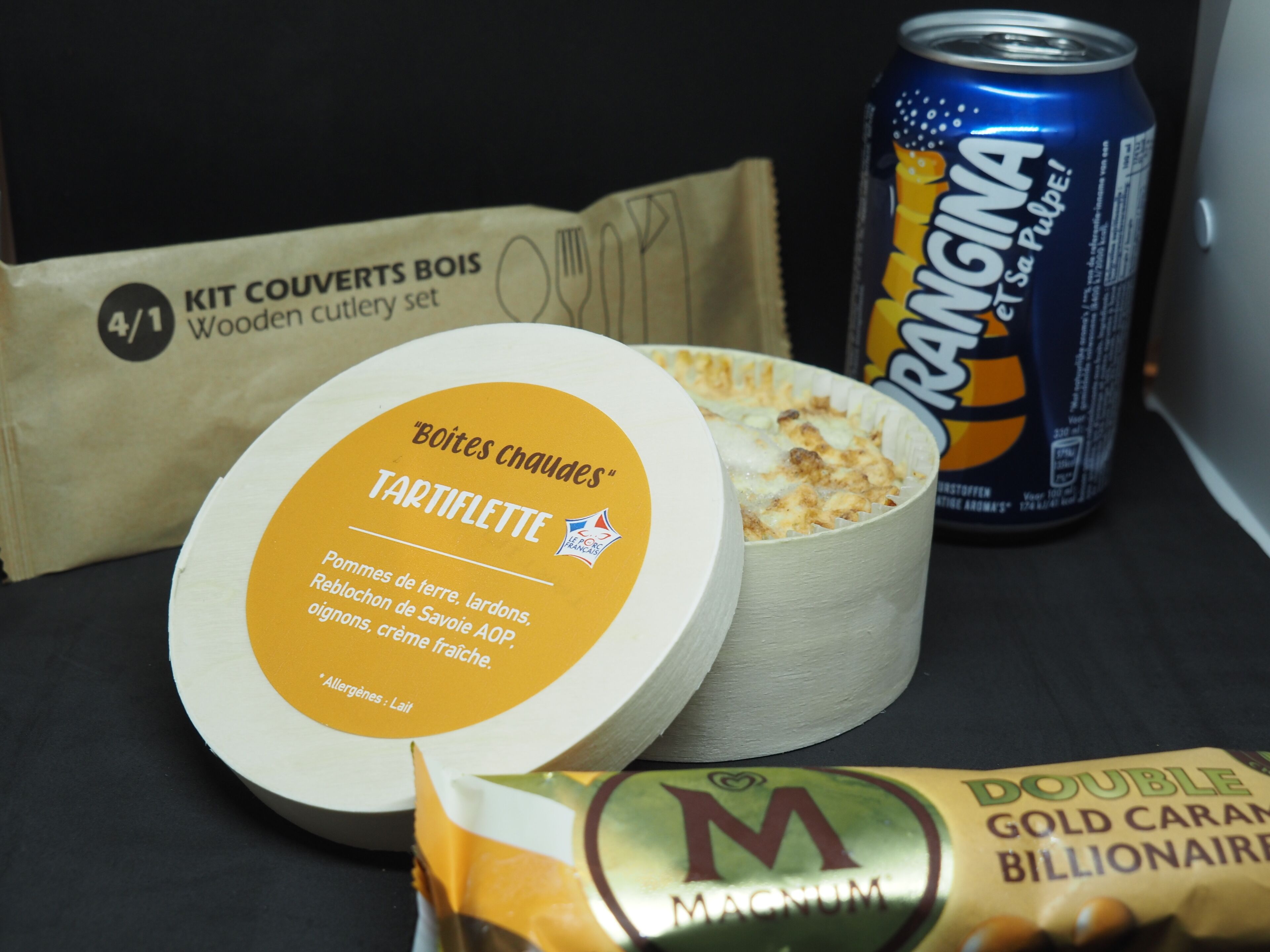 Une planche à découper en bois, une boîte de boisson Tang et un paquet de barres chocolatées Magnum Gold Caramel Billionaire.