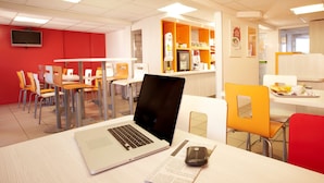 A modern dining area with a laptop on a table, surrounded by chairs and a counter with food items. - Premiere Classe Saumur (Saumur)