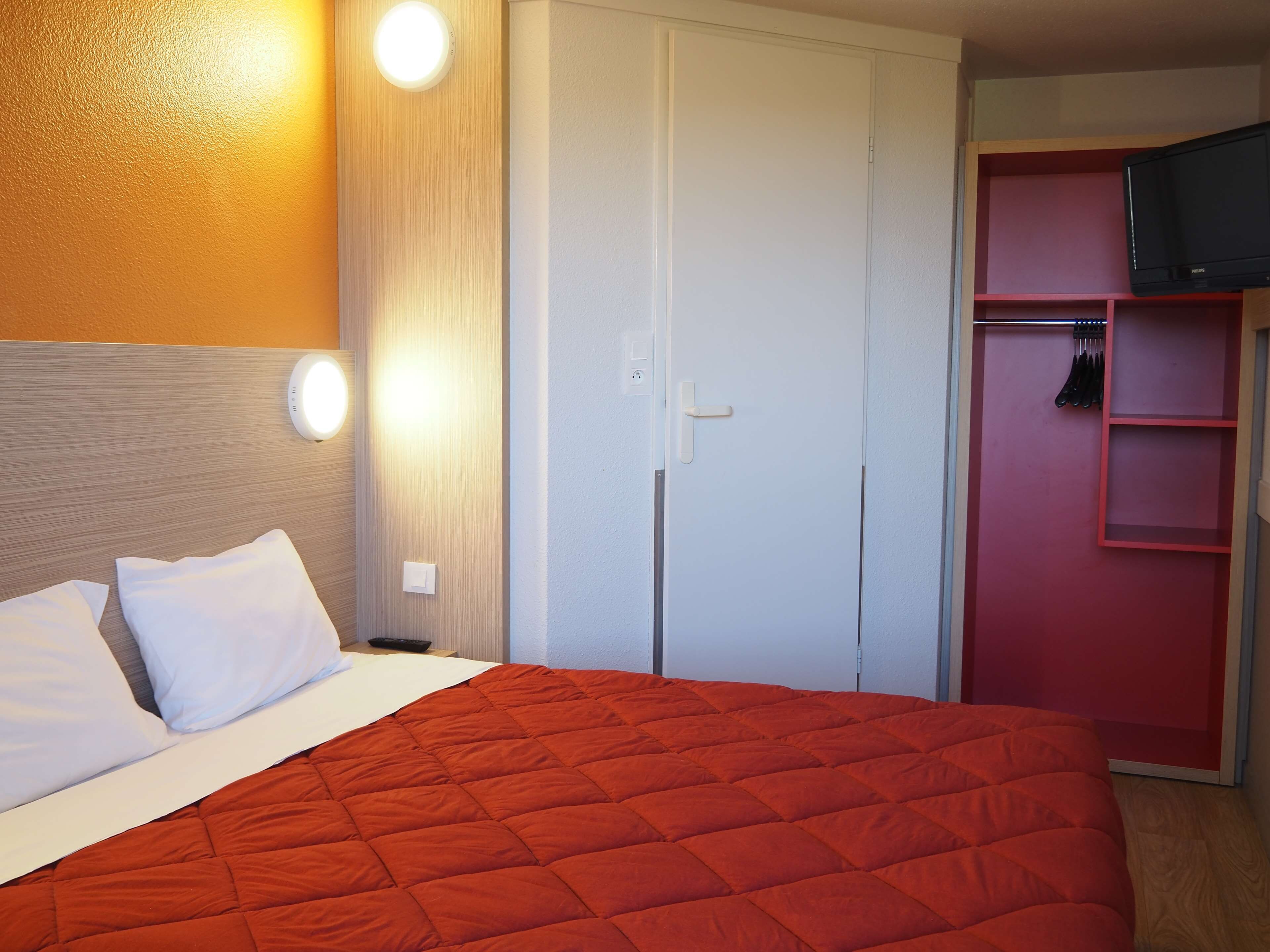 Habitación de hotel con cama, armario y televisor.