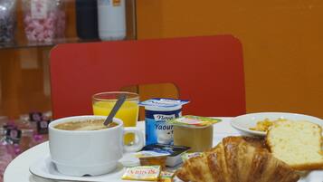 Un plateau de petit-déjeuner avec un croissant, du pain, une tasse de café, un verre de jus d’orange et un pot de yaourt.