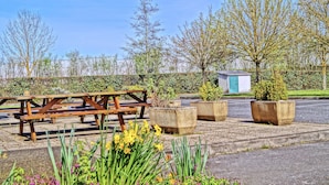 A picnic table and planters in a garden area with a hedge and trees in the background. - Premiere Classe Saumur (Saumur)
