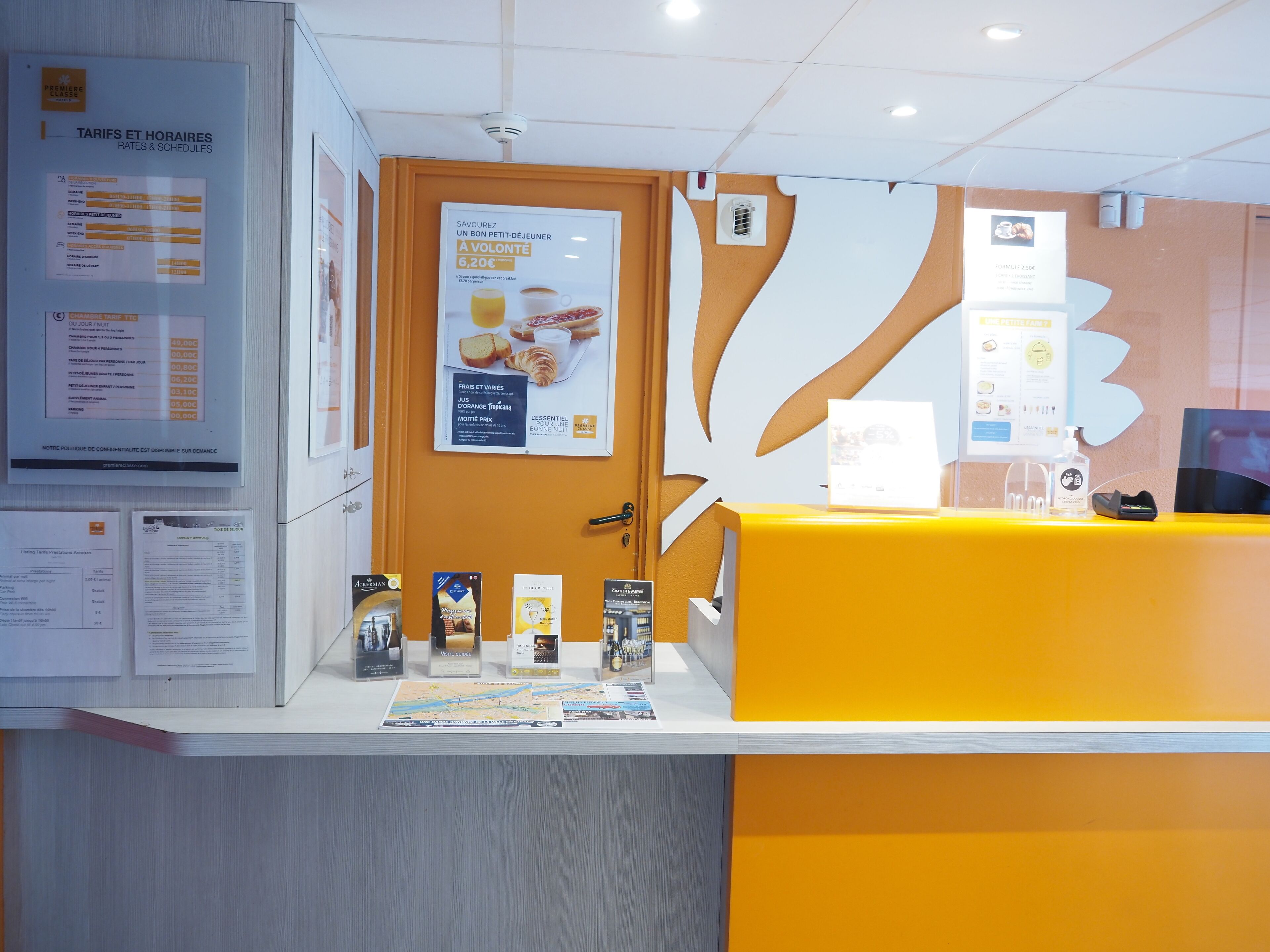 Un comptoir d’accueil avec un plan de travail jaune, des affiches d’information et un panneau d’affichage où sont accrochées diverses annonces.