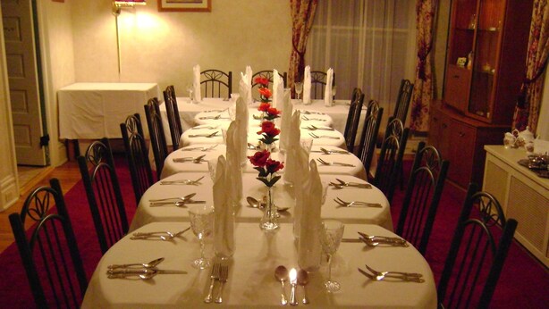 A long dining table set with white tablecloths, multiple chairs, and a vase with red flowers. - Four Creeks Bed & Breakfast (Girard)