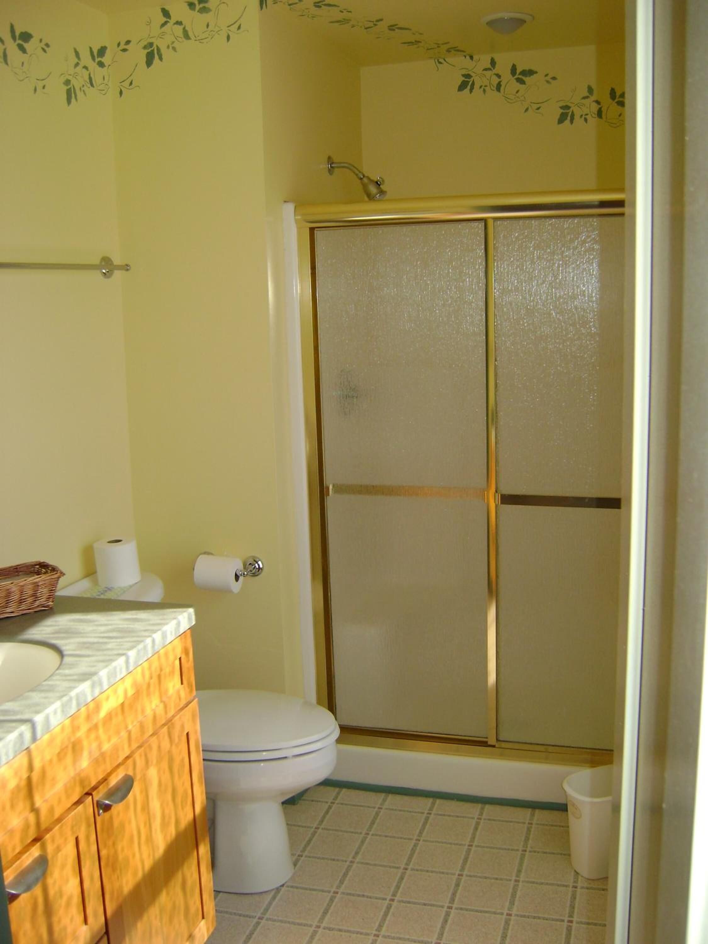 A bathroom with a toilet, a wooden cabinet, a shower with a glass door, and a wall-mounted toilet paper holder.