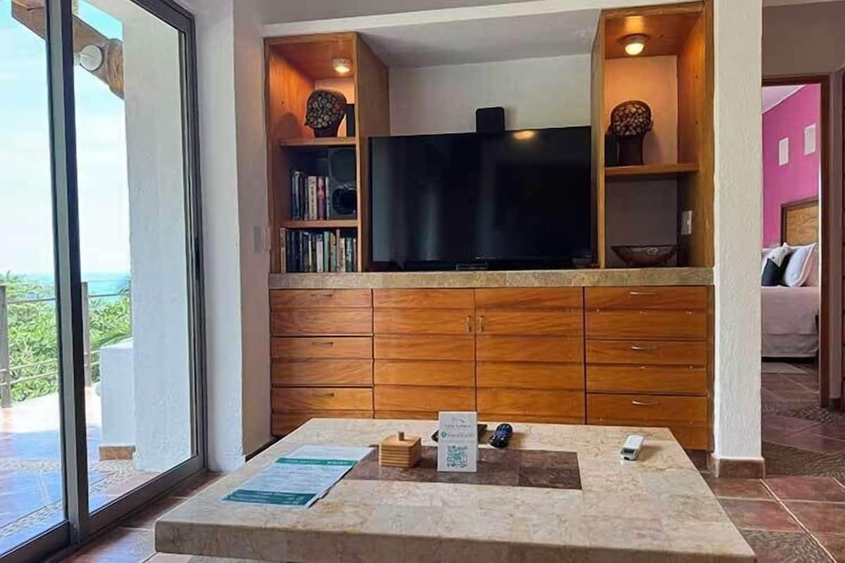 Una sala de estar moderna con un televisor de pantalla plana, armarios de madera y una pequeña mesa con un menú.