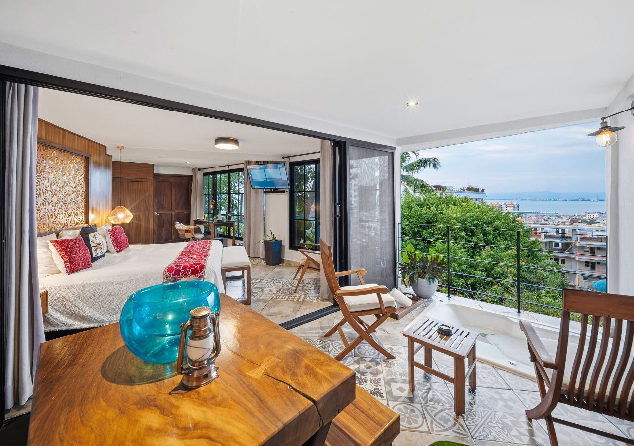 Une chambre d’hôtel moderne avec balcon, un grand lit, une table en bois et une vue sur la ville.
