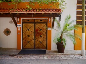 Una entrada de edificio con una puerta grande y ornamentada, una planta en maceta y un cartel con el nombre 'TASTE'.
