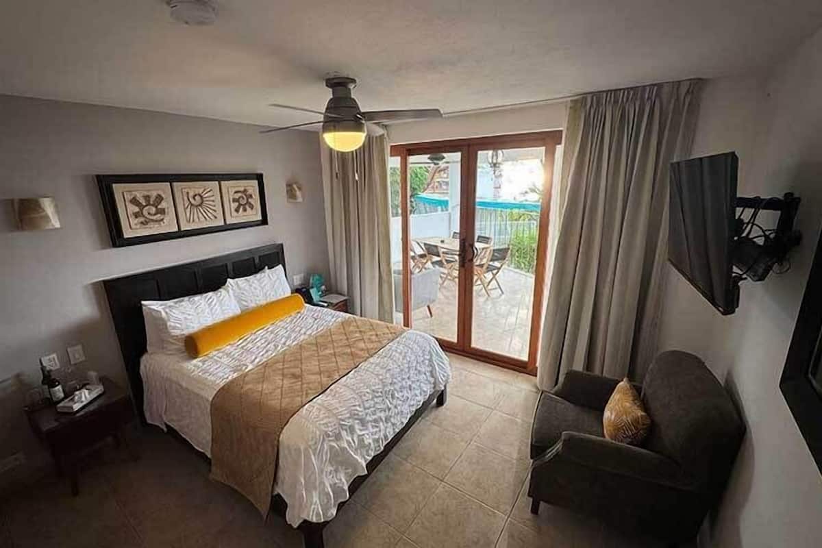 Habitación de hotel con cama, televisión, silla y balcón con mesa y sillas.