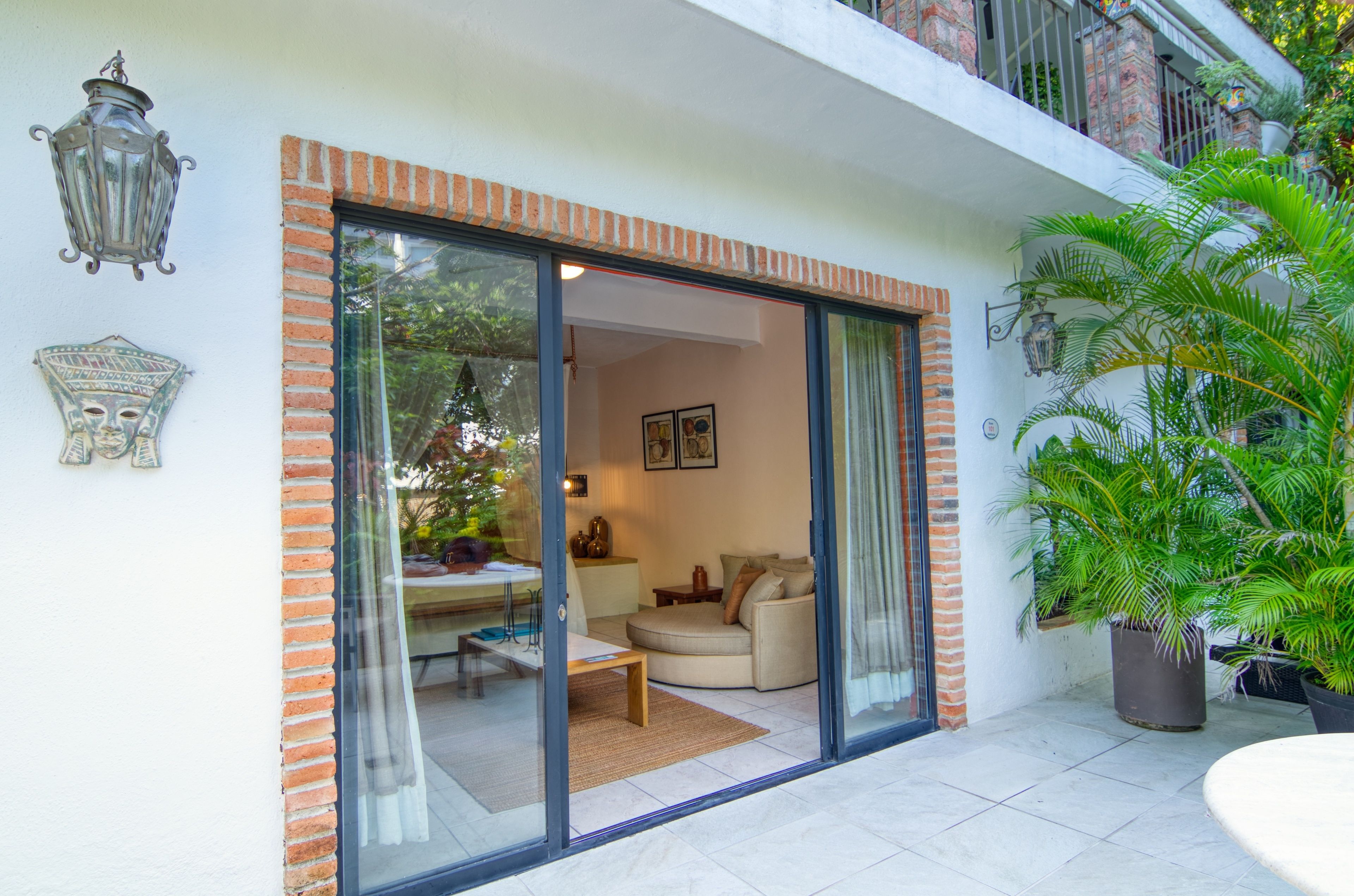 Una sala de estar moderna con un ventanal que da a un balcón, un comedor con mesa y sillas, y una planta grande en maceta.
