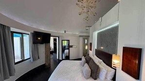 A modern bedroom with a large bed, a flat-screen TV mounted on the wall, and a ceiling light fixture.