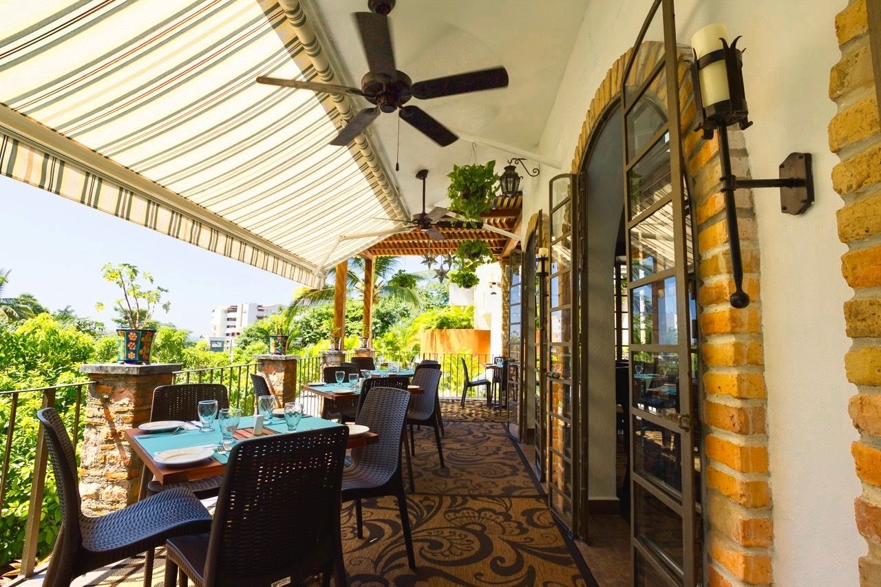 Un área de comedor al aire libre con mesas y sillas, un ventilador de techo y una pared de ladrillo.