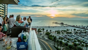 A balcony overlooking a sunset with a view of the beach and pier.