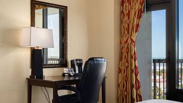 Une chambre d’hôtel avec un lit, un bureau avec une lampe, une chaise, une machine à café et une fenêtre avec des rideaux.