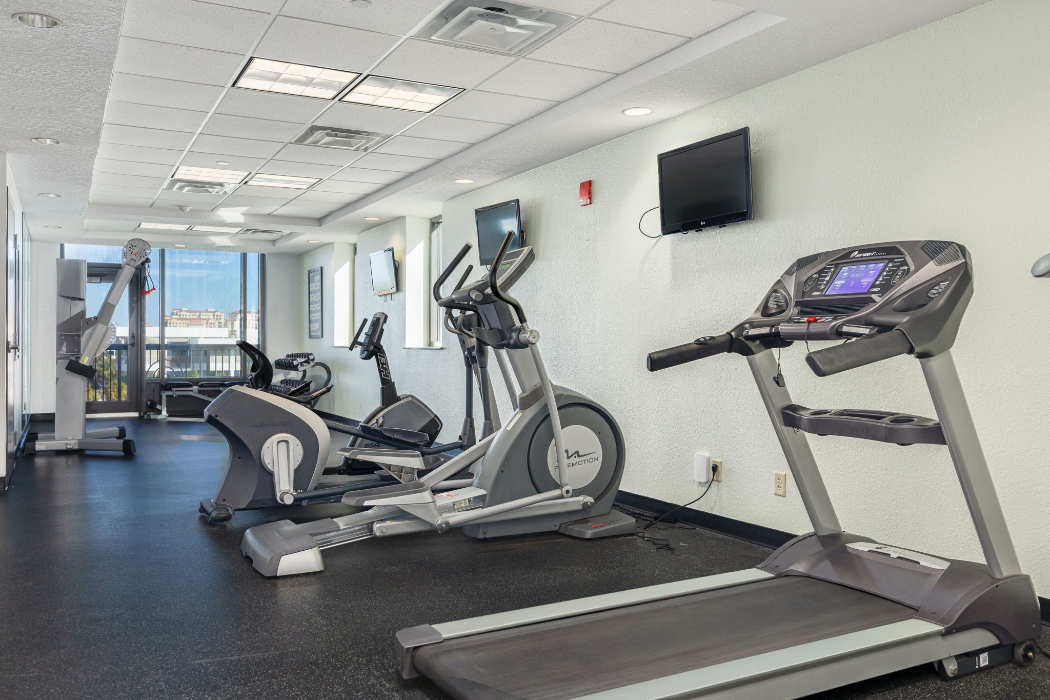 Un gimnasio con cintas de correr, elípticas y una bicicleta estática.