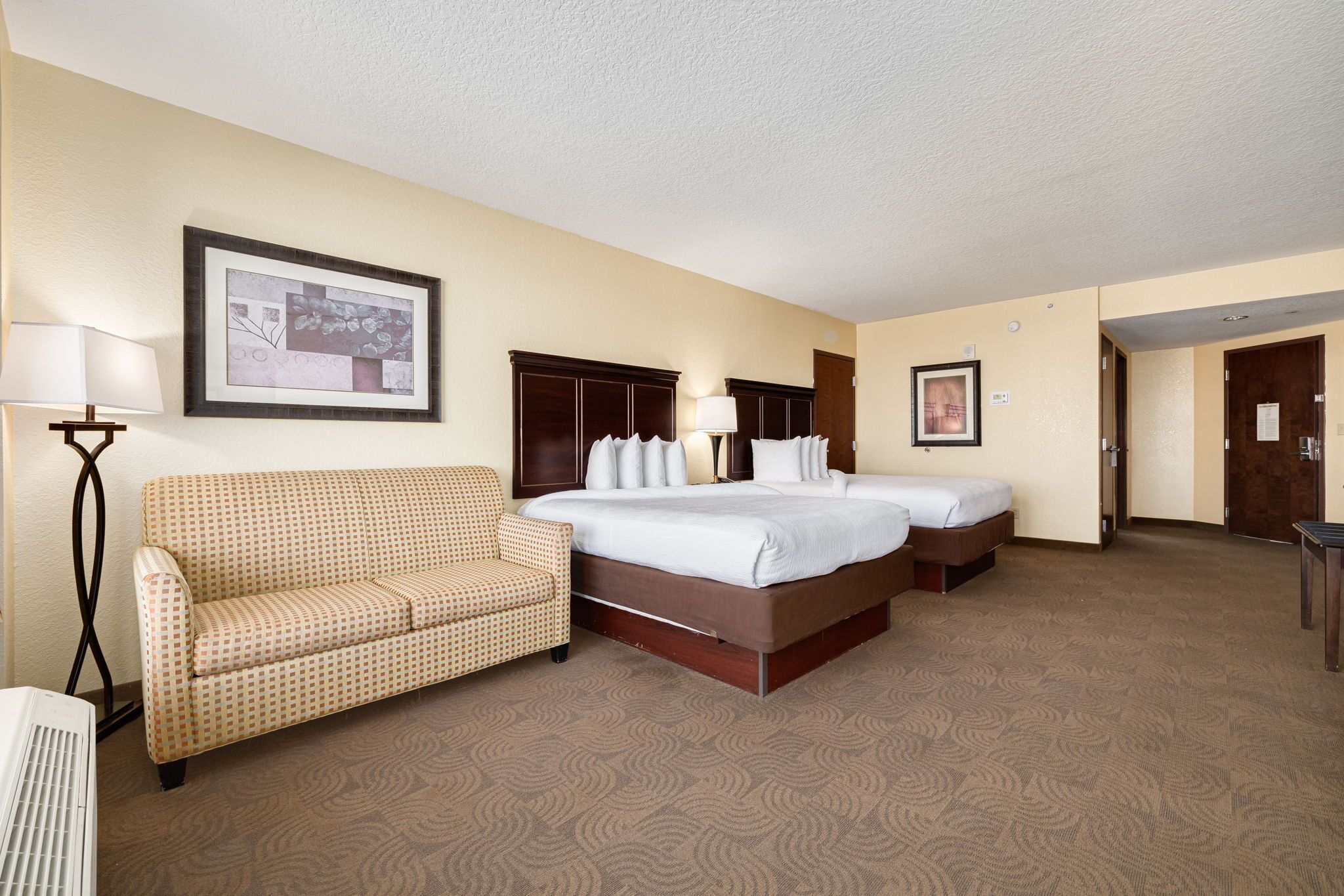 A hotel room with a bed, a sofa, a desk, and a lamp.