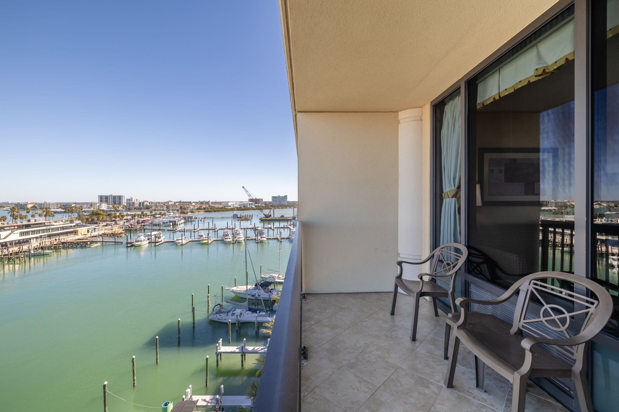 A balcony with two chairs overlooking a marina with boats and a cityscape in the background.