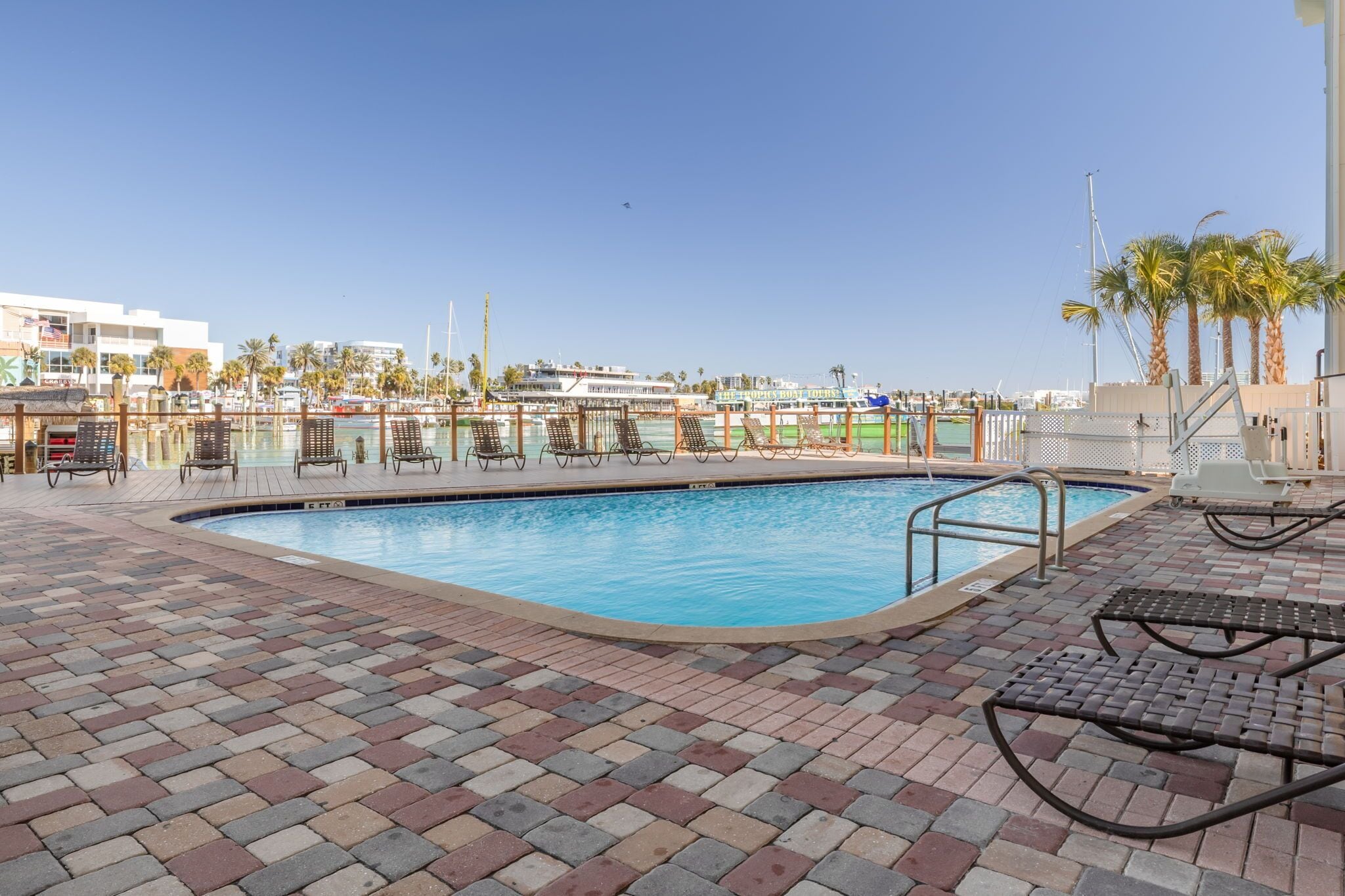 Une piscine entourée de chaises longues et de palmiers, le tout bordé d’une terrasse en briques.