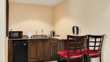 Cocina pequeña con armarios de madera oscura, un microondas negro, una cafetera y un teléfono. Hay dos sillas con cojines rojos.