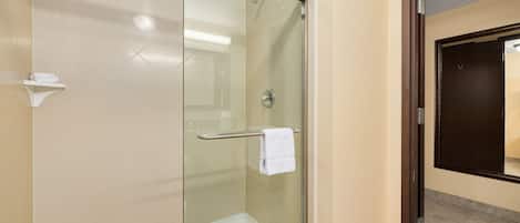 A glass-enclosed shower area with a white towel on a rack, beige walls, and a dark door in the background.