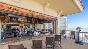 A Bacardi bar with a view of the ocean, outdoor seating, and a high-rise building in the background.