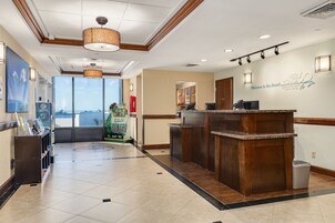 Un área de recepción con un mostrador de madera, un amplio ventanal con vistas a la playa y un letrero dando la bienvenida a los huéspedes al Hotel Pier 60 Marina.