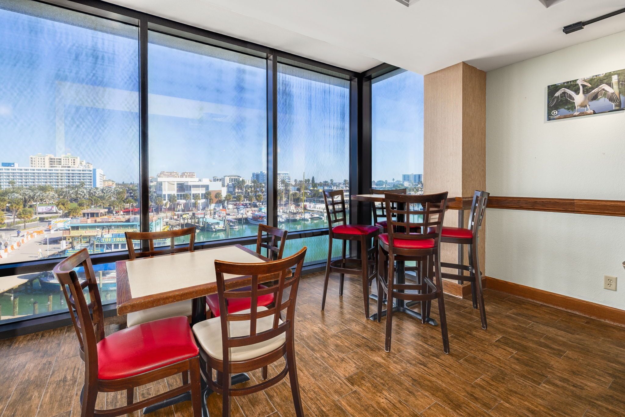Comedor con mesas y sillas de madera, ventanas amplias que ofrecen vistas a un puerto deportivo y al paisaje urbano.
