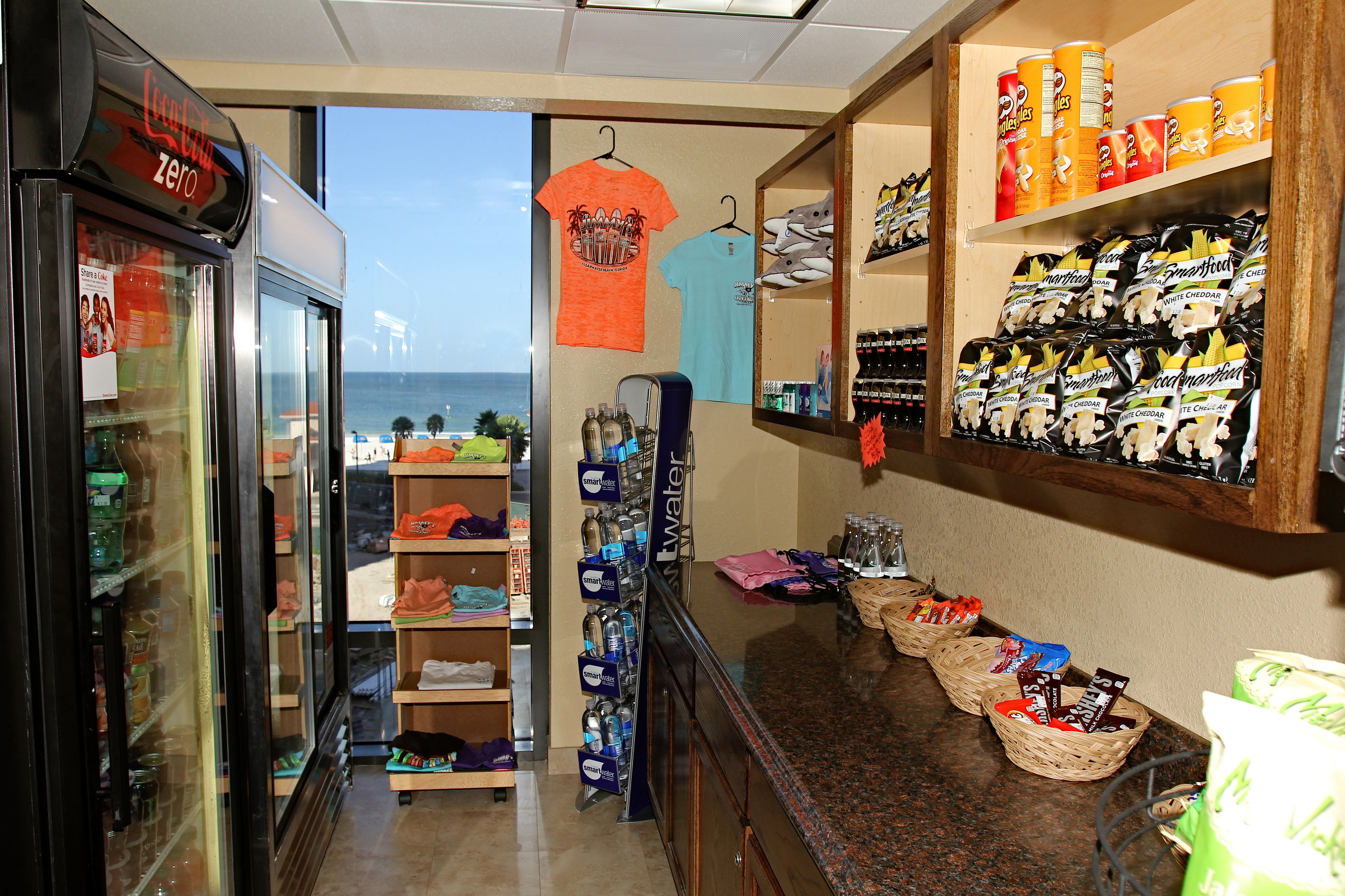 Una tienda con estantes llenos de botanas y bebidas, una exhibición de camisetas y un refrigerador de Coca-Cola.