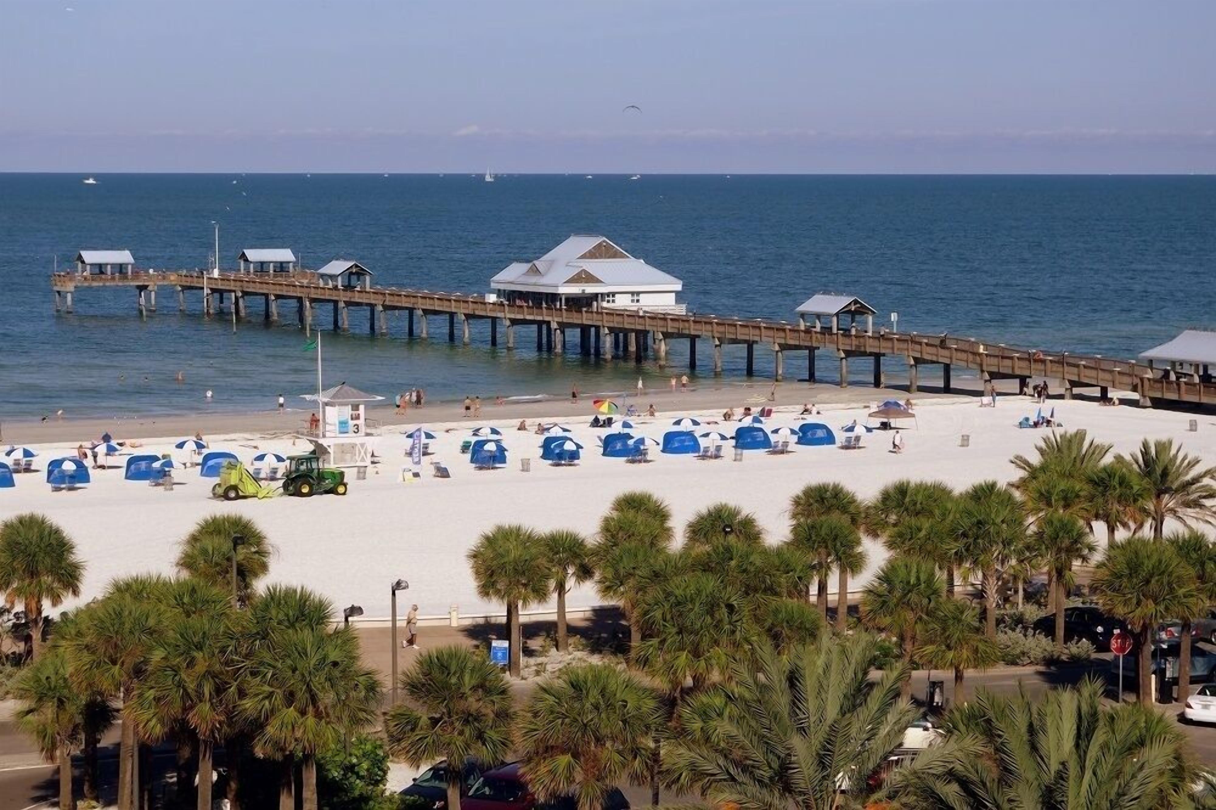 Een strand met een houten pier, strandparasols en palmbomen.