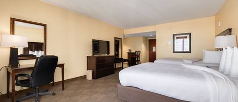 A hotel room with a large bed, a desk with a chair, a television, and a dresser.