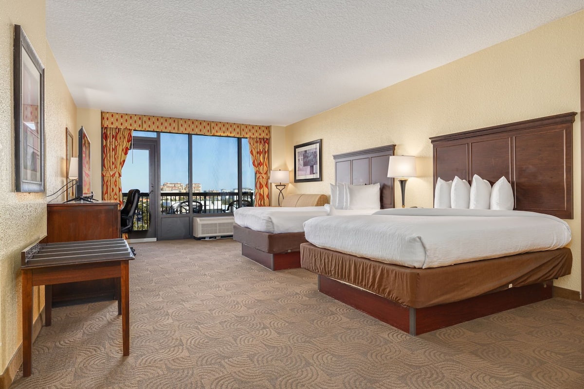 A hotel room with two beds, a desk, a chair, a window with a view, and a balcony.