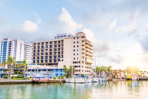 Un hotel frente al agua con varios balcones, un puerto deportivo lleno de barcos y palmeras.