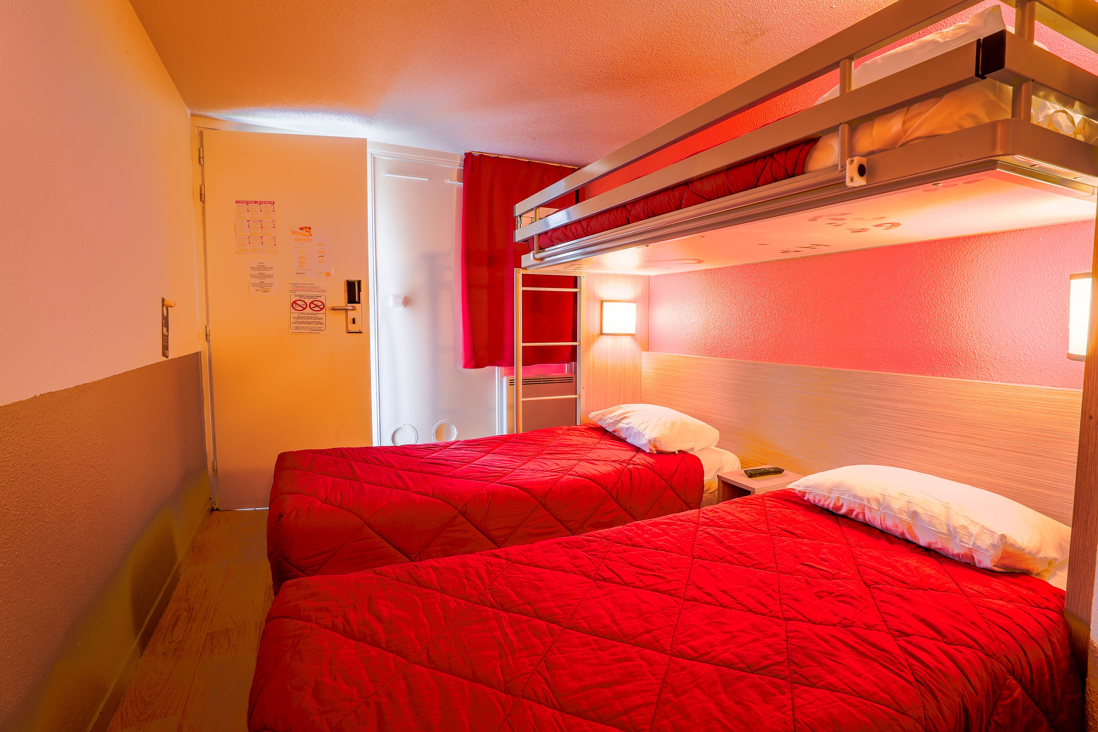 A room with two beds, each with a red bedspread, a wooden headboard, and a nightstand with a lamp.