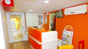 A reception area with a bright orange counter, a white wall-mounted air conditioner, and a magazine rack. - Premiere Classe Saint Quentin (Saint-Quentin)