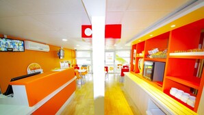 A brightly lit restaurant with orange and white decor, a counter, and tables with chairs. - Premiere Classe Saint Quentin (Saint-Quentin)