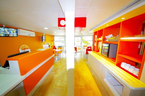 A brightly lit restaurant with orange and white decor, a counter, and tables with chairs. - Premiere Classe Saint Quentin (Saint-Quentin)