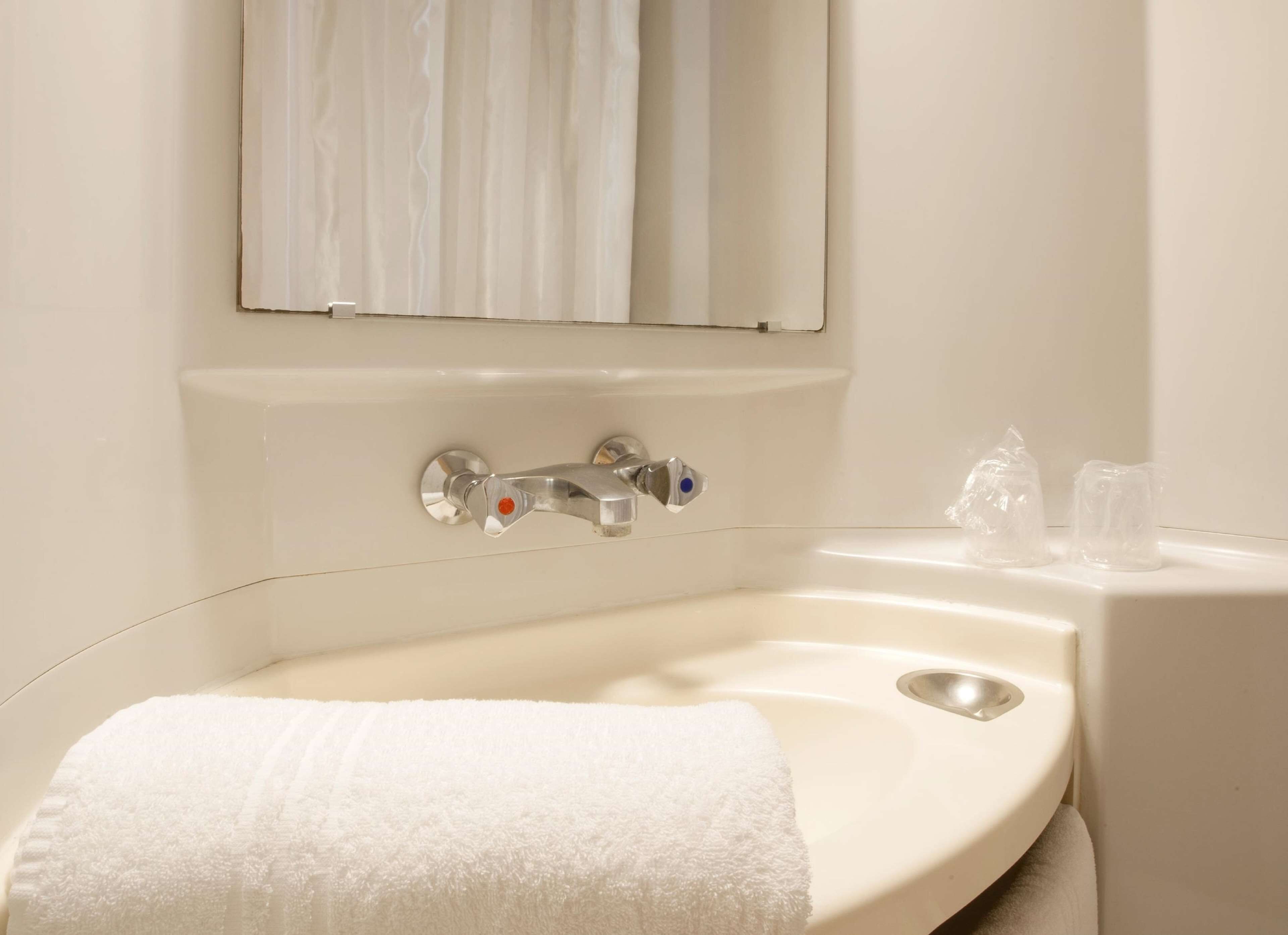 Un baño con un lavamanos blanco, un espejo y una toalla.