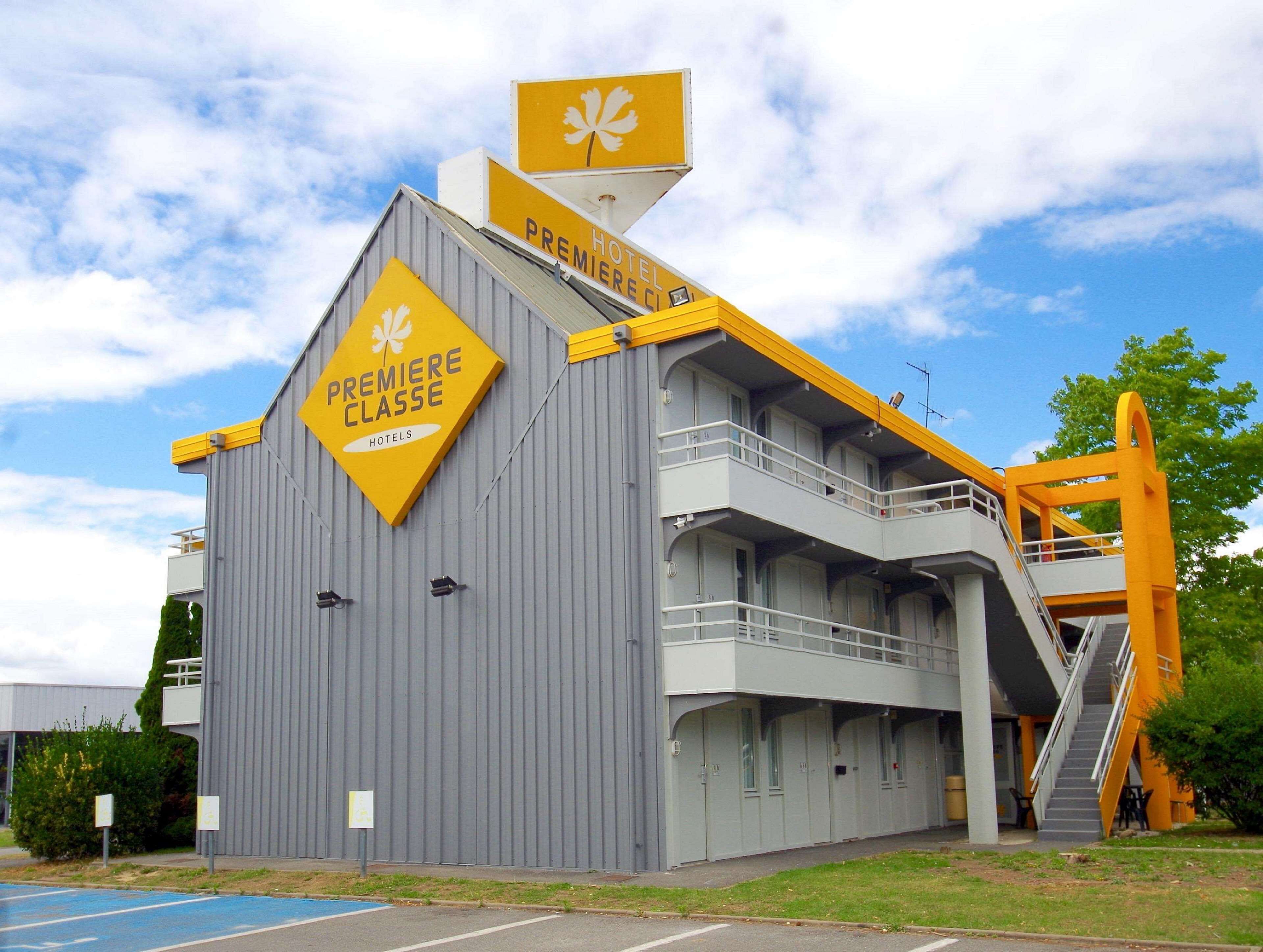 Un edificio de hotel con un llamativo letrero amarillo que dice "PREMIERE CLASSE HOTELS" y una escalera que conduce a un nivel superior.