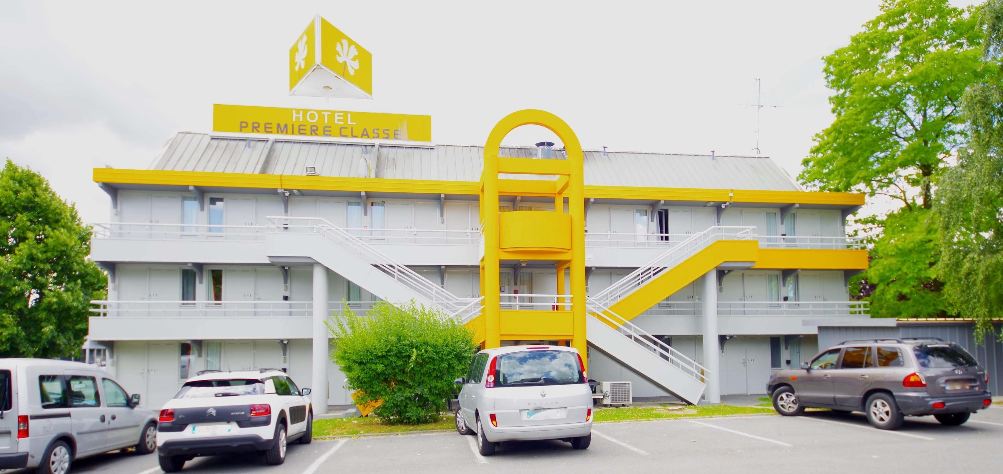 A hotel with a prominent yellow and white color scheme, multiple parking spaces, and a staircase leading to the entrance.