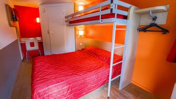 A bunk bed with a red bedspread, a desk with a chair, and a wall-mounted TV.