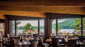 A restaurant with wooden interior and large windows offering a view of a lake and forest.