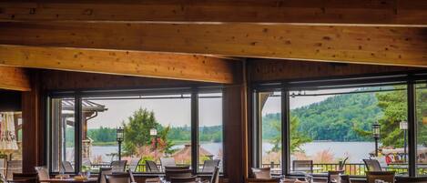 Restaurante con interior de madera y ventanas amplias que ofrecen vistas a un lago y un bosque.