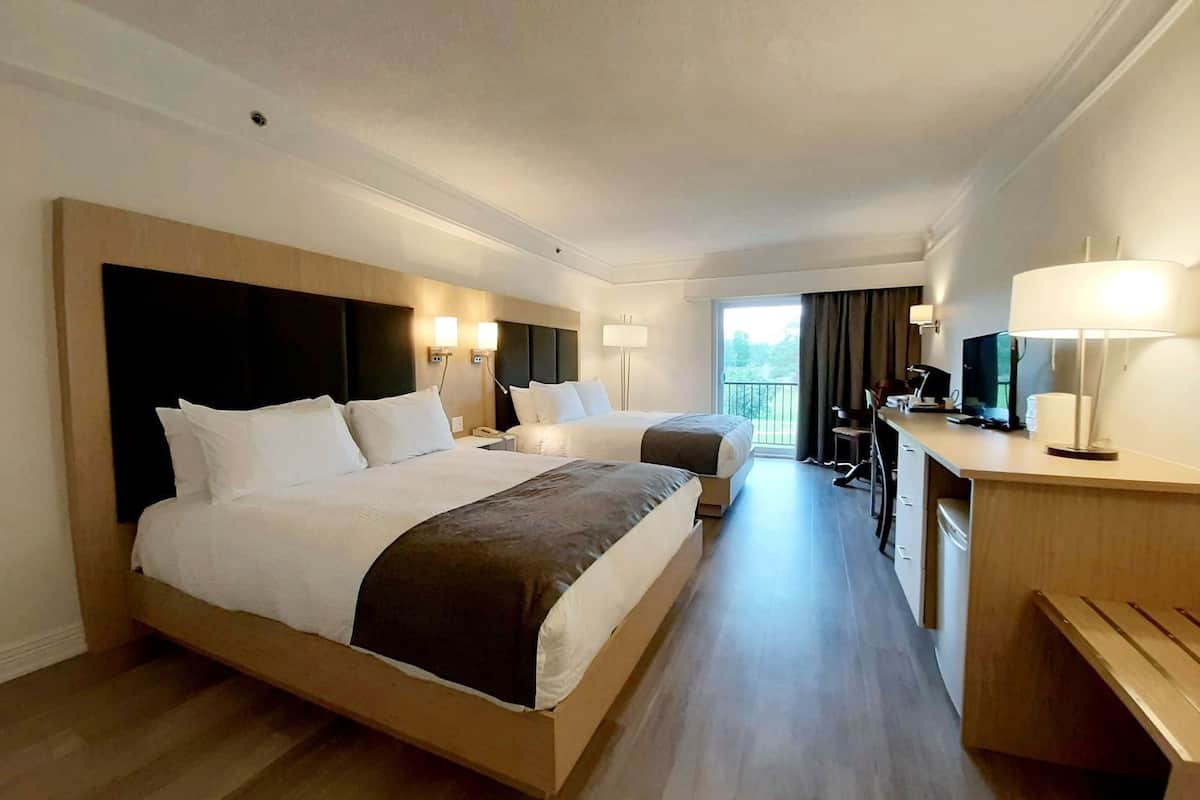 Quarto de hotel com duas camas, uma escrivaninha, uma cadeira, televisão e varanda com vista.