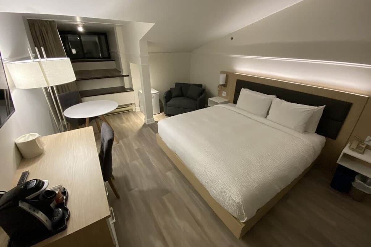 Quarto de hotel com cama, escrivaninha, cadeira, televisão e luminária.
