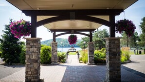 A covered outdoor area with stone pillars, hanging flower baskets, and a view of a lake.