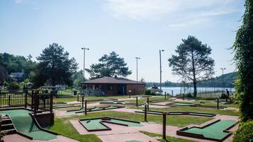 A miniature golf course with multiple green putting areas and a small building in the background.