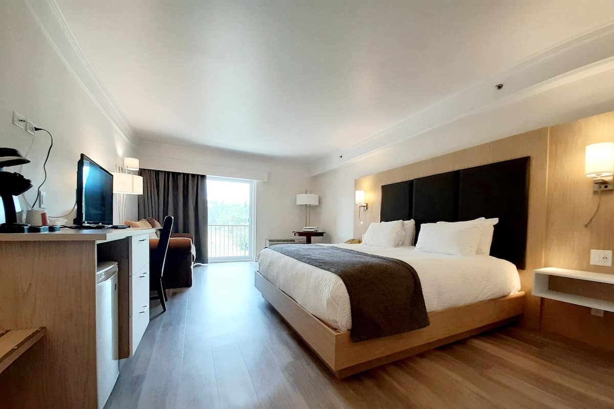 Quarto de hotel moderno com uma cama grande, uma escrivaninha com um computador, uma cadeira e vista para o exterior.