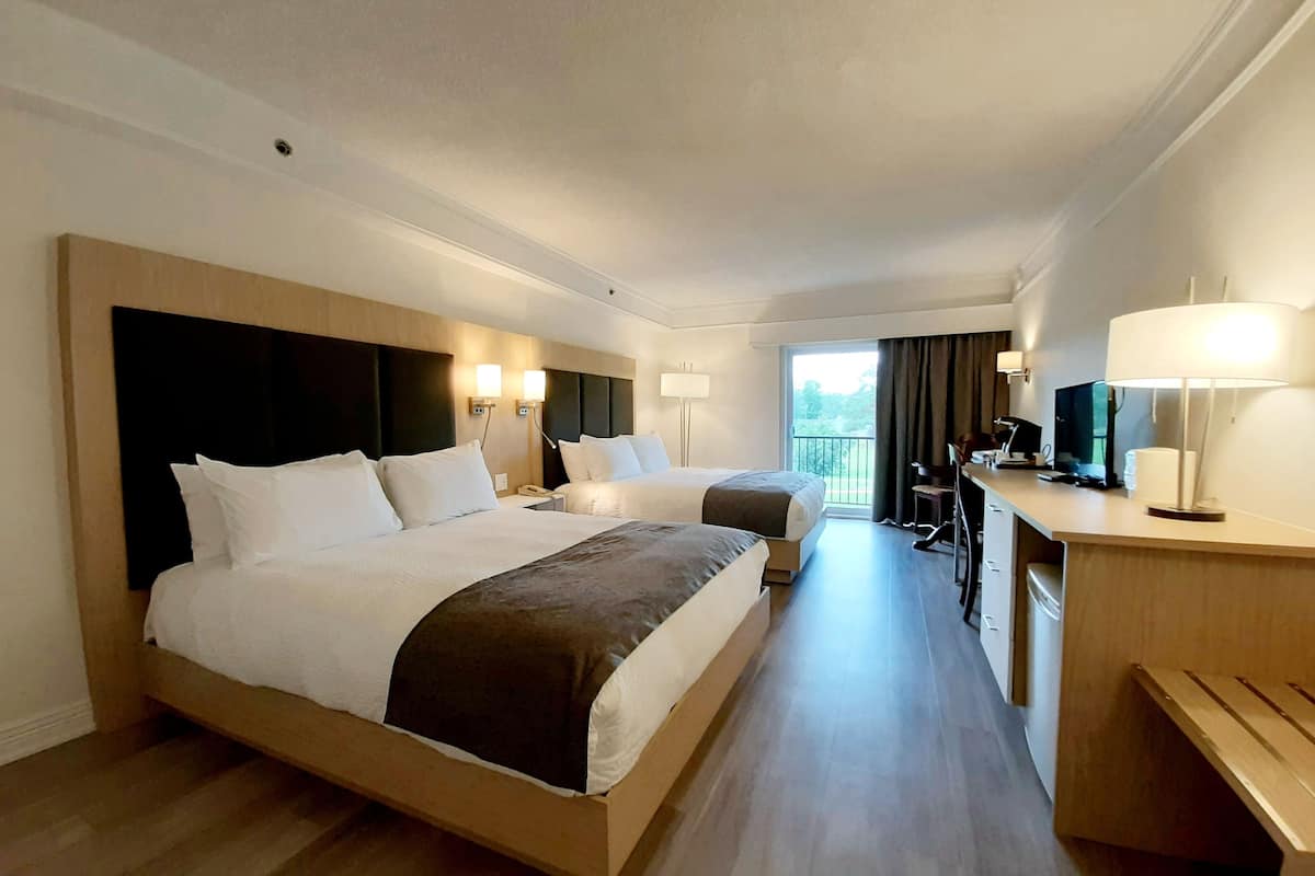 Quarto de hotel com duas camas, uma escrivaninha com cadeira, televisão e varanda com vista.