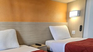 Une chambre d’hôtel avec deux lits, chacun recouvert d’une couverture rouge et blanche, dotée d’une tête de lit en bois, d’une table de chevet avec une télécommande et d’une lampe fixée au mur.